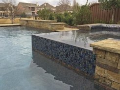 Iridescent Glass Tile Spa with Pebble Sheen and Brass Spillways in Frisco